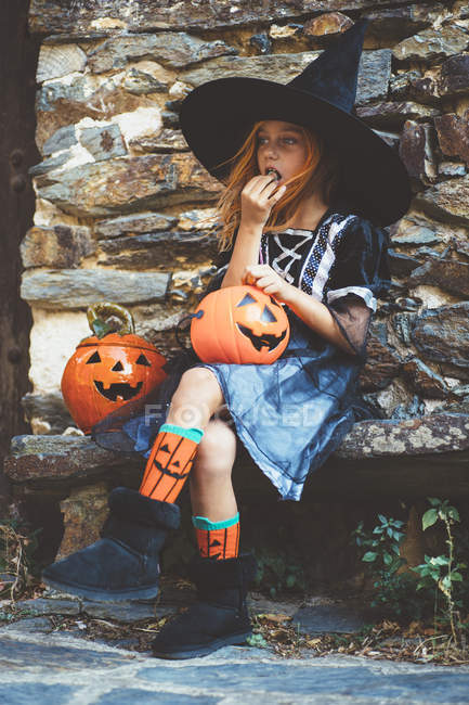 Mädchen isst Halloween-Leckerbissen auf Bank — Stockfoto