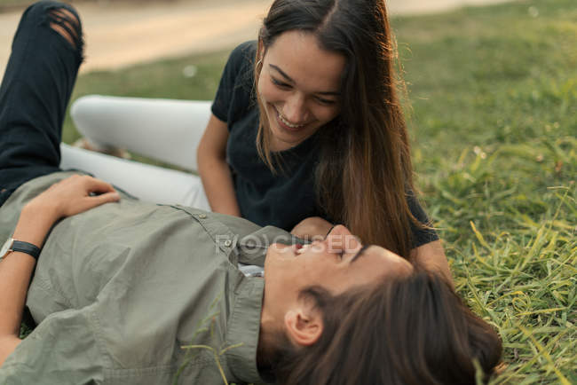 Junges lächelndes Paar, das auf dem Gras liegt und sich gegenseitig ansieht und zusammen Spaß hat. l — Stockfoto