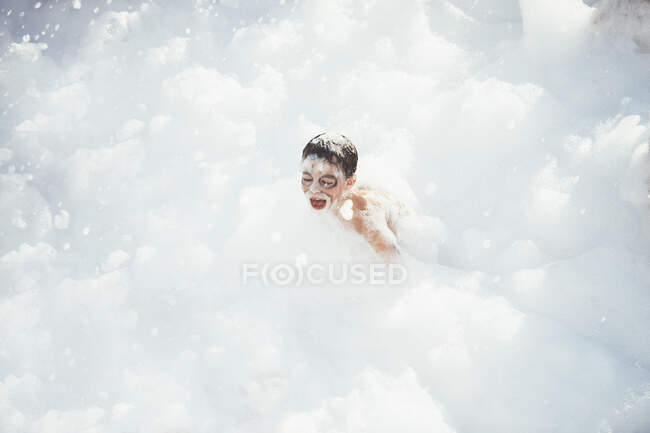 Cheerful kid playing in white foam — Stock Photo