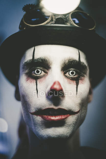 Close-up of scary man with clown Halloween make-up and hat looking at camera — Stock Photo