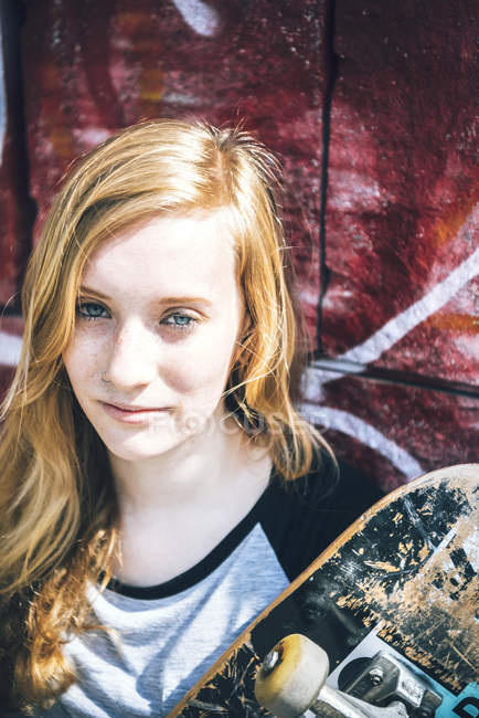 Молодая женщина-скейтбордистка позирует у стены граффити — стоковое фото