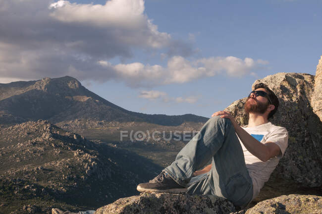 Розслаблений молодий чоловік засмагає на вершині гори на заході сонця — стокове фото