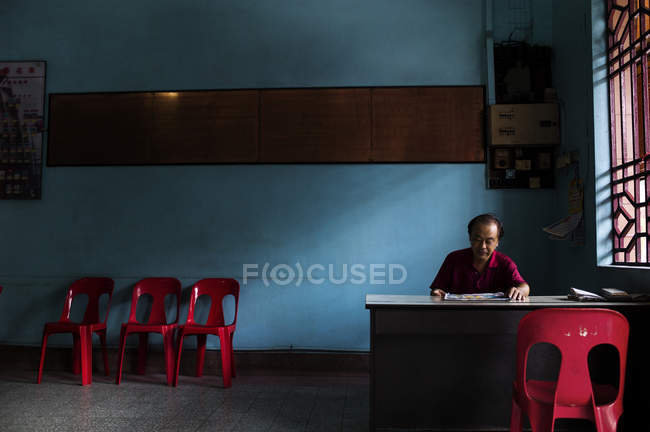 KAULA LUMPUR, MALASIA - 21 ABRIL, 2016: Hombre maduro sentado en la mesa en el pasillo cerca de la ventana con sillas a lo largo de la pared  . - foto de stock