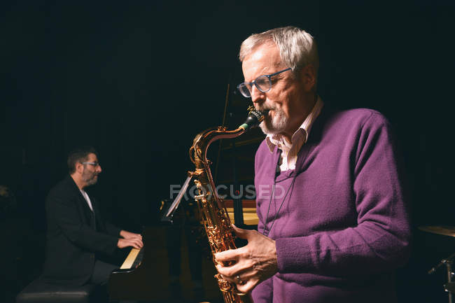 Senior homme jouant du saxophone avec bande — Photo de stock