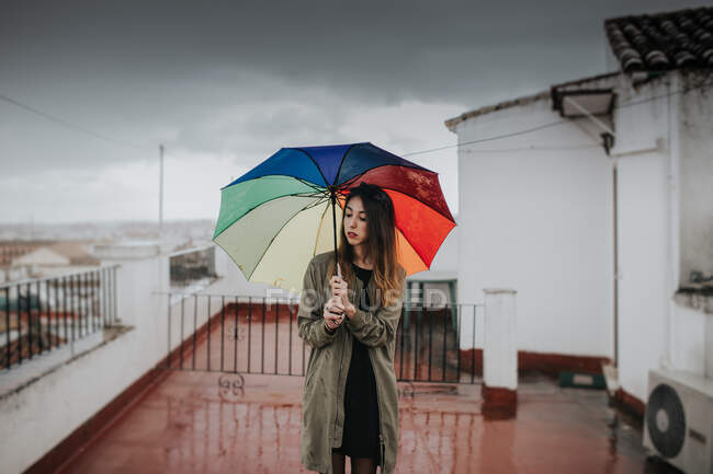 Giovane bruna in piedi sul tetto dell'edificio con ombrello colorato arcobaleno. Copyspace. — Foto stock