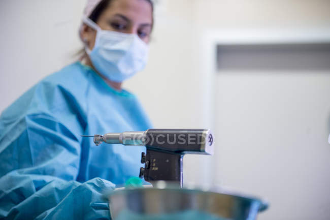 Portrait of female doctor in mask looking at surgical drill — Stock Photo