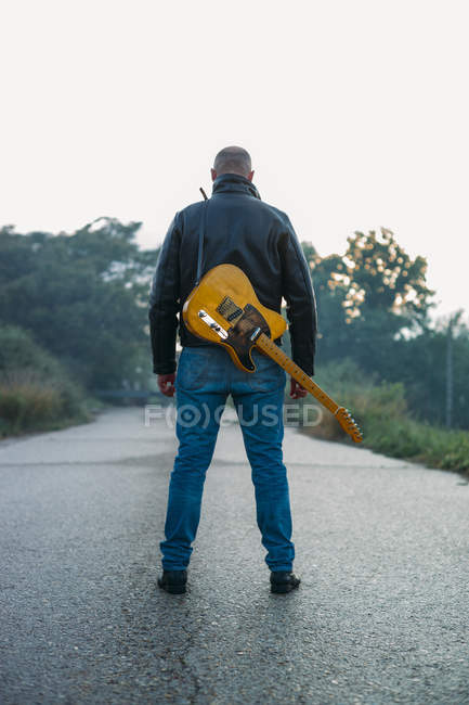 Vista posteriore di uomo adulto che trasporta chitarra elettrica in piedi su strada vuota . — Foto stock