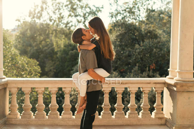 Side view of boyfriend holding girlfriend on hands over ornate marble parapet — Stock Photo