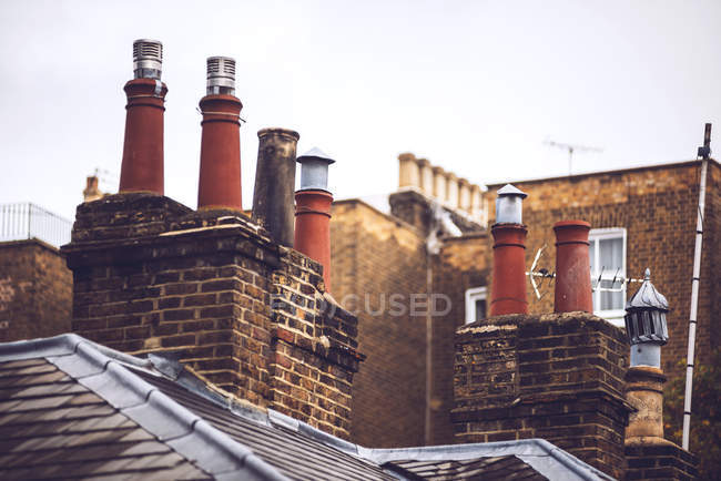 Красные кирпичные дымоходы на крышах против голубого неба — стоковое фото