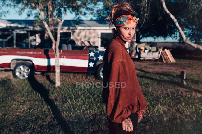 Молода жінка в вуличному стилі стоїть на відкритому повітрі з вантажівкою на фоні і дивиться на камеру . — стокове фото