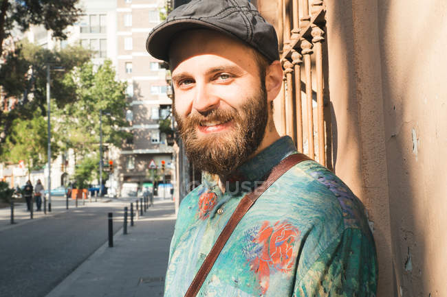 Hombre barbudo alegre sonriendo a la cámara en la calle de la ciudad - foto de stock