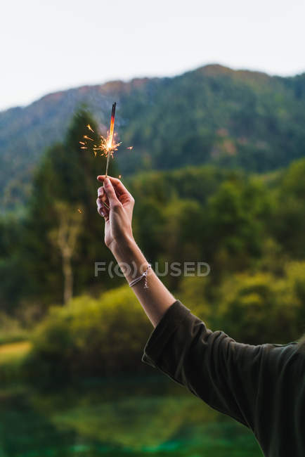 Crop hand holding sparkler on nature — Stock Photo