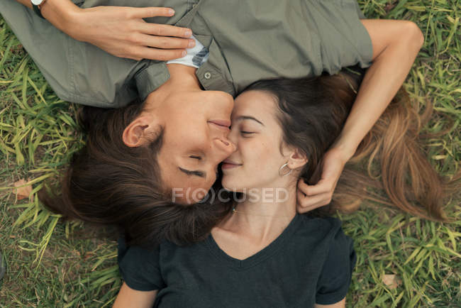 Blick von oben auf ein Paar, das im Gras liegt und sich mit geschlossenen Augen umarmt. — Stockfoto