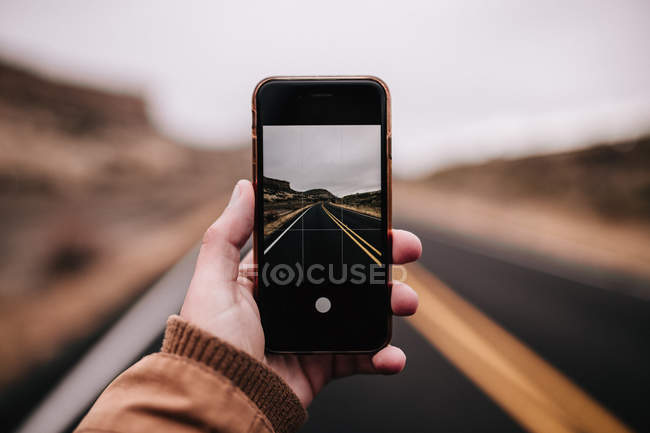 Recortar la mano sosteniendo el teléfono inteligente y rodaje escena carretera - foto de stock