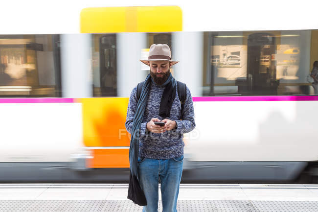 Vista frontal do homem de chapéu que navega smartphone sobre o trem em movimento no fundo — Fotografia de Stock