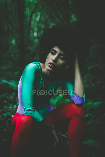 Чуттєва дівчина з кучерявим волоссям, сидячи в лісі і дивлячись на камеру — стокове фото