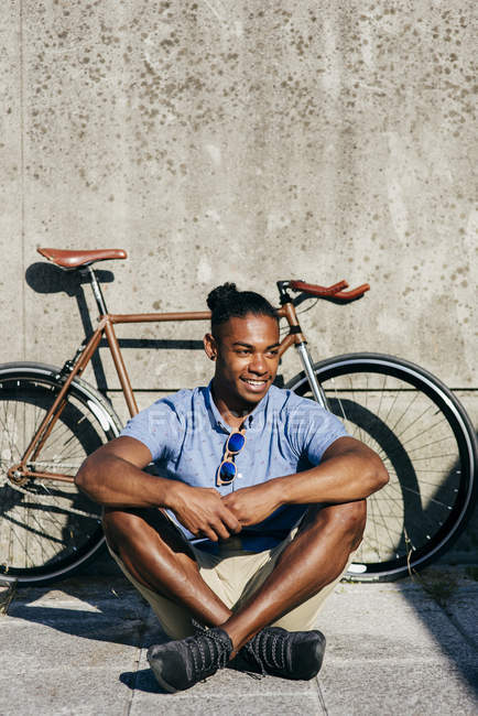 Uomo sorridente seduto vicino alla bicicletta — Foto stock
