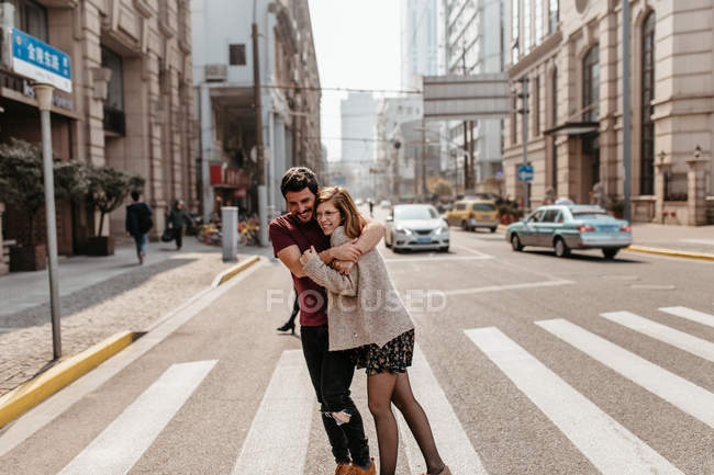Young couple hugging each other while walking trough pedestrian crosswalk. — Stock Photo