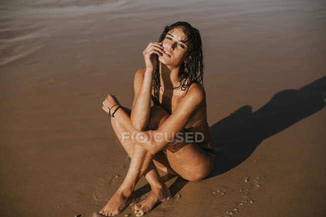 Retrato de mujer en topless con el pelo mojado escondiendo el pecho con las rodillas y mirando a la cámara - foto de stock