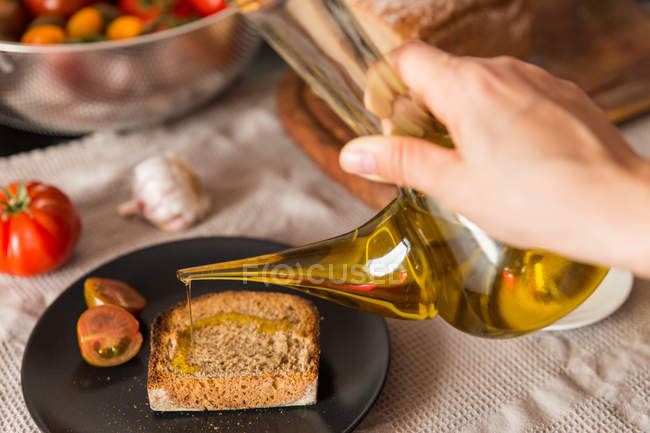 Persona versando olio sul pane tostato — Foto stock