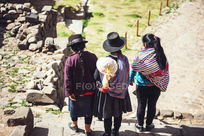Вид сзади на троих женщин с ребенком, идущих по руинам инков — стоковое фото