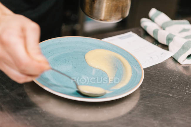 Close up view of hand with spoon decorating plate with cream on table at restaurant kitchen — Stock Photo