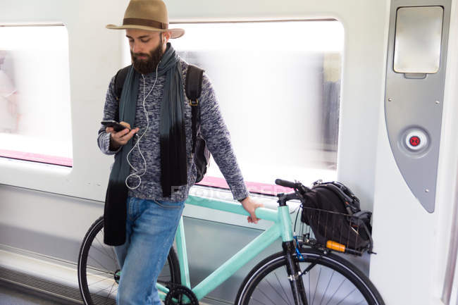 Barbudo hombre en sombrero celebración fixie bicicleta y el teléfono inteligente de navegación en tren . - foto de stock