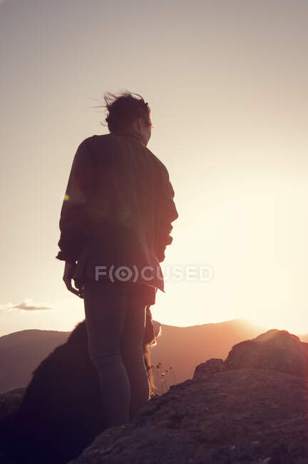 Young woman fondles her pet during a beautiful sunset at the top of the mountain — Stock Photo