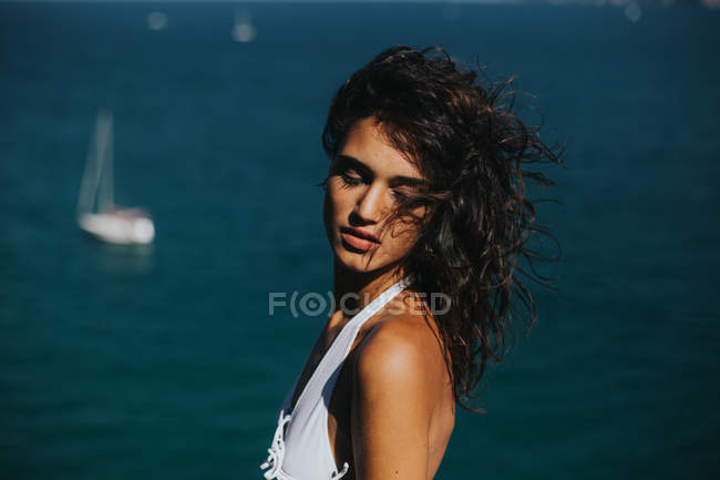 Retrato de chica morena con los ojos cerrados posando sobre el paisaje marino con yates flotantes - foto de stock