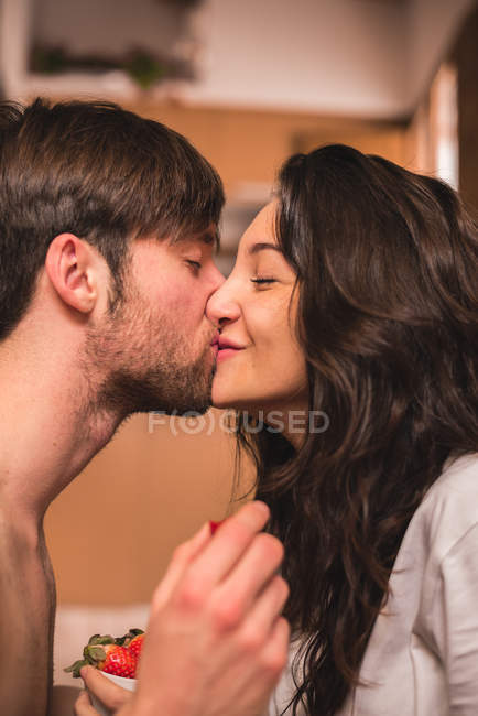 Cheerful couple kissing and holding strawberry. — Stock Photo