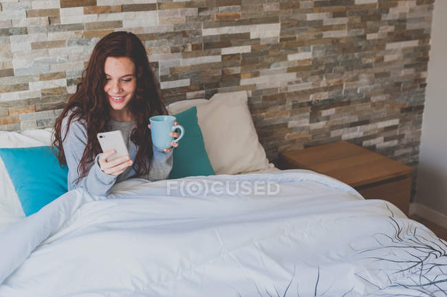 Menina deitada na cama e usando smartphone — Fotografia de Stock