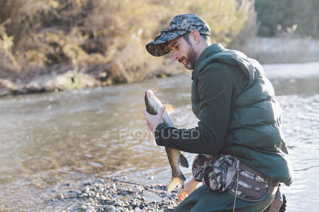 Fisher sitting on shore and admiring catch. — Stock Photo