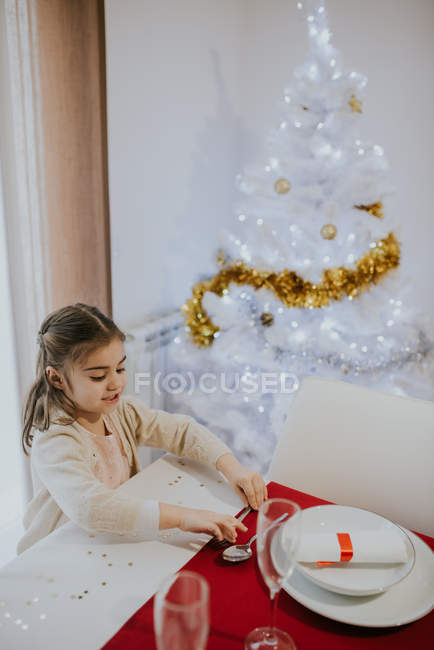 Vista de ángulo alto de la niña sirviendo cuchara en la mesa de Navidad cerca del árbol de Navidad blanco . - foto de stock