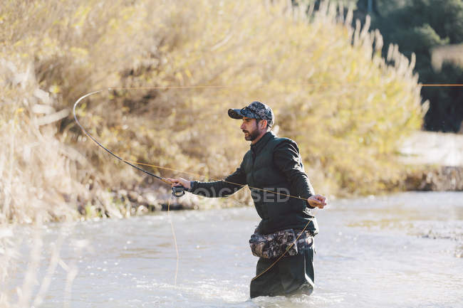 Vista lateral del hombre de pie en el agua y la pesca con caña - foto de stock