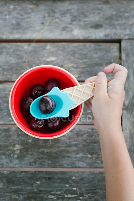 Mano de niña tomando cereza con cuchara de tazón - foto de stock