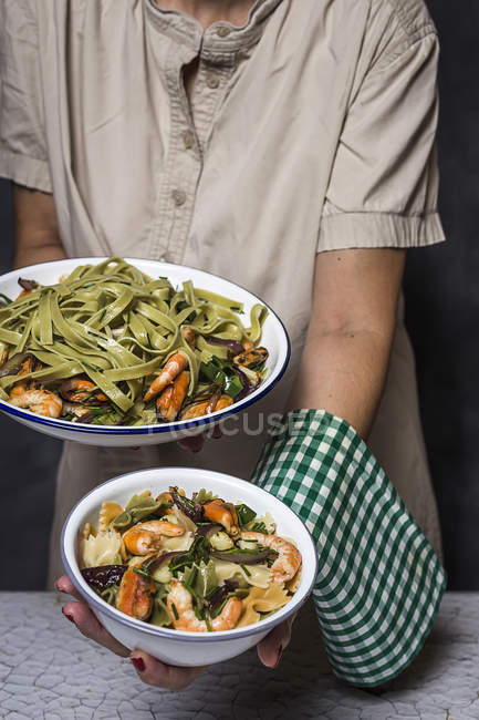 Midsection of woman showing plates of italian green tagliatelle with seafood — Stock Photo