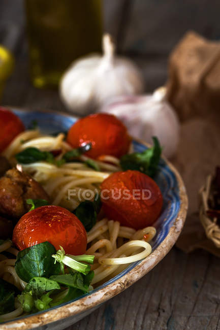 Crop image of plate of pasta with basil and cherry tomatoes on rustic wooden table with garlic — Stock Photo