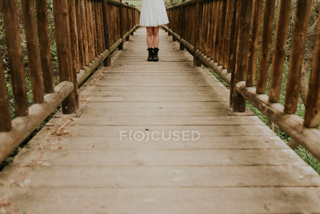 Нижняя часть девушки в белом платье позирует на деревянном мосту — стоковое фото