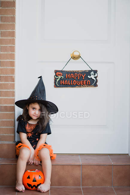 Chica en traje de bruja sentado en el porche - foto de stock