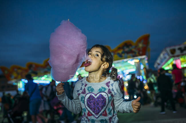 Uma menina comendo rosa doce-fio dental no luna-parque — Fotografia de Stock