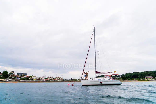 Distant view of two girls posing on yacht nose in bay — Stock Photo