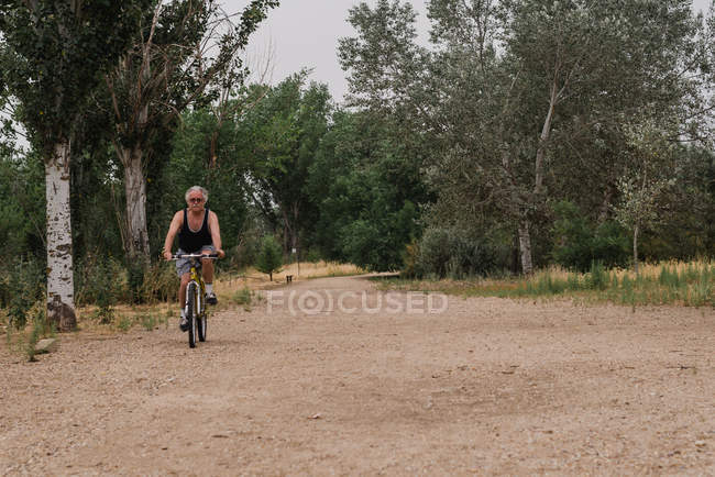 Vista frontal do homem sênior andar de bicicleta na estrada do campo — Fotografia de Stock