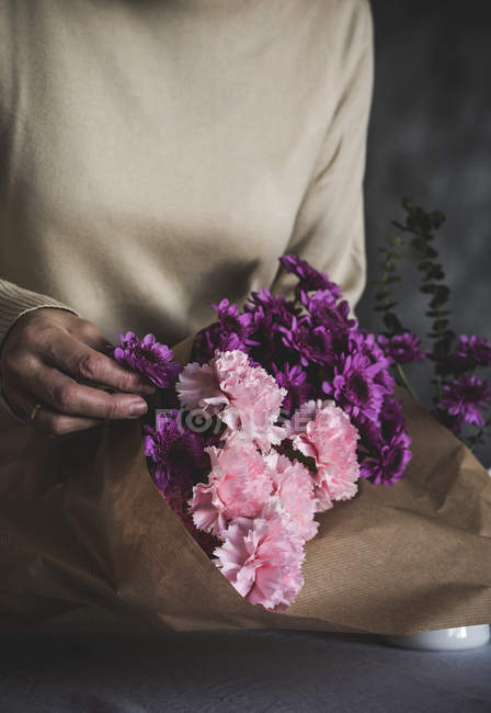 Close-up vista do florista feminino mãos embrulhando buquê de flores em papel artesanal na mesa — Fotografia de Stock