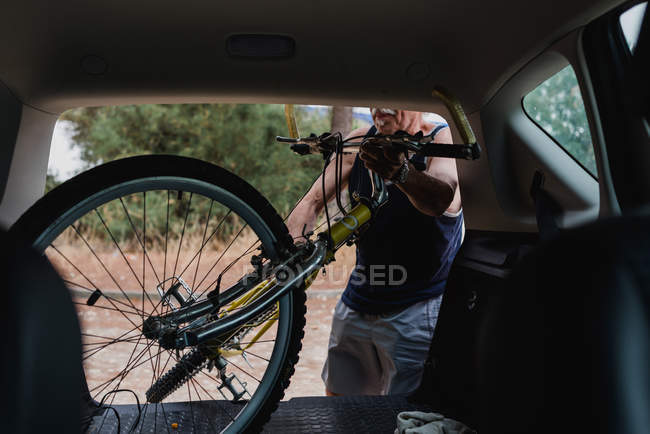 Uomo anziano mettere la bicicletta nel bagagliaio dell'auto in campagna — Foto stock