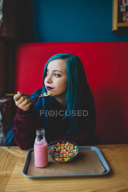 Retrato de adolescente con pelo azul comiendo cereales en la cafetería - foto de stock