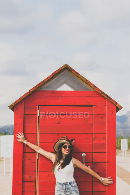 Portrait of cheerful brunette woman wearing cowboy hat and sunglasses closing changing cabin with arms — Stock Photo