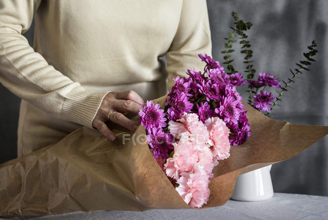 Mid section of female florist wrapping bouquet of flowers in craft paper on table — Stock Photo