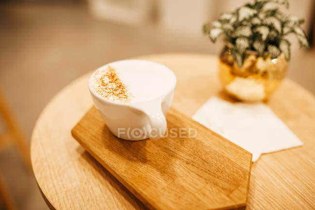Крупный план чашки капучино на деревянной доске на столе с растением — стоковое фото
