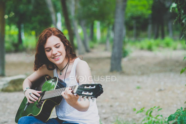 Retrato de menina sardenta feliz com cabelo vermelho tocando guitarra na floresta — Fotografia de Stock