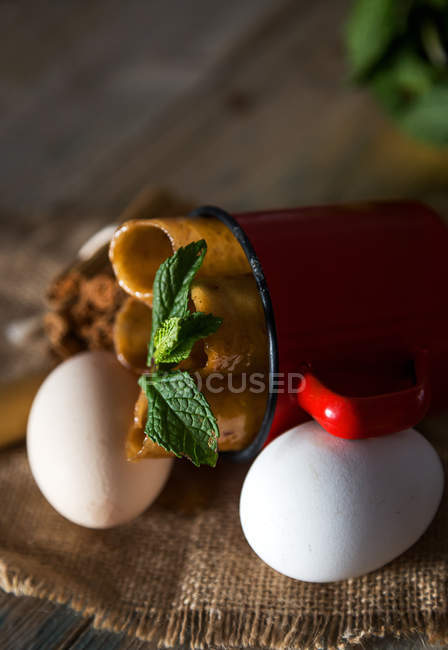 Vista cercana de la taza con tubos de masa dulce y hojas de menta acostadas en sacos con huevos - foto de stock